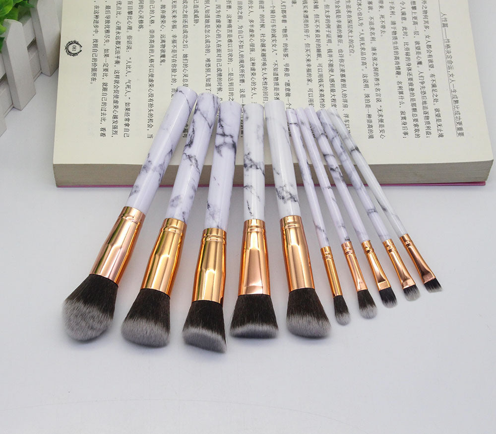 Set of makeup brushes with marble handle design on a white surface.