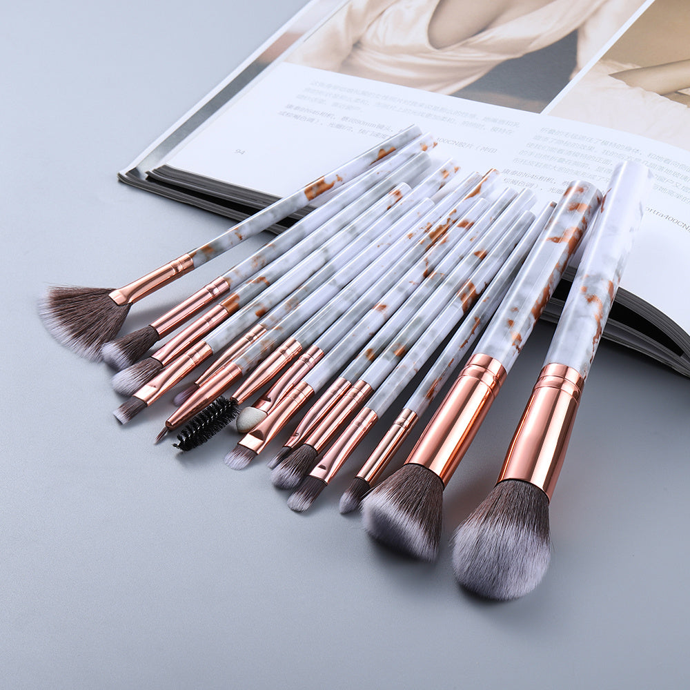 Set of makeup brushes with rose gold handles on a light gray surface