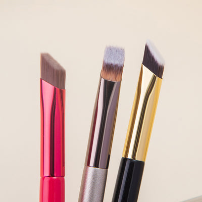Three makeup brushes with colorful handles on a light beige background