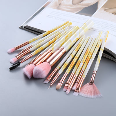 Set of makeup brushes with yellow and white handles on a light gray surface.