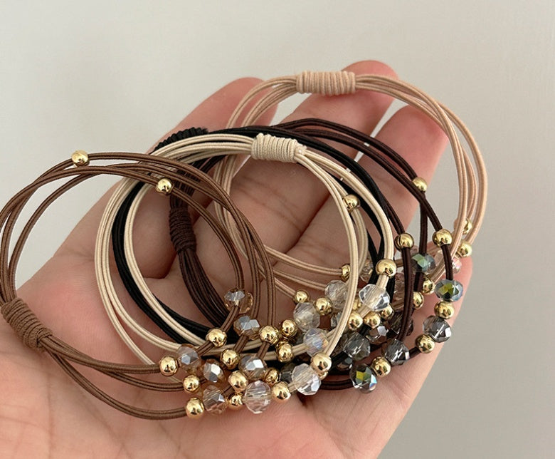 Close-up of Durable Hair Rope Adult Hair Elastic Bands in various colors with gold and crystal beads, held in a hand for detail view.
