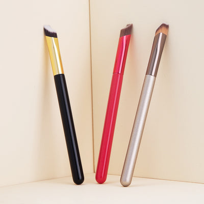Three makeup brushes with black, red, and silver handles on a beige background